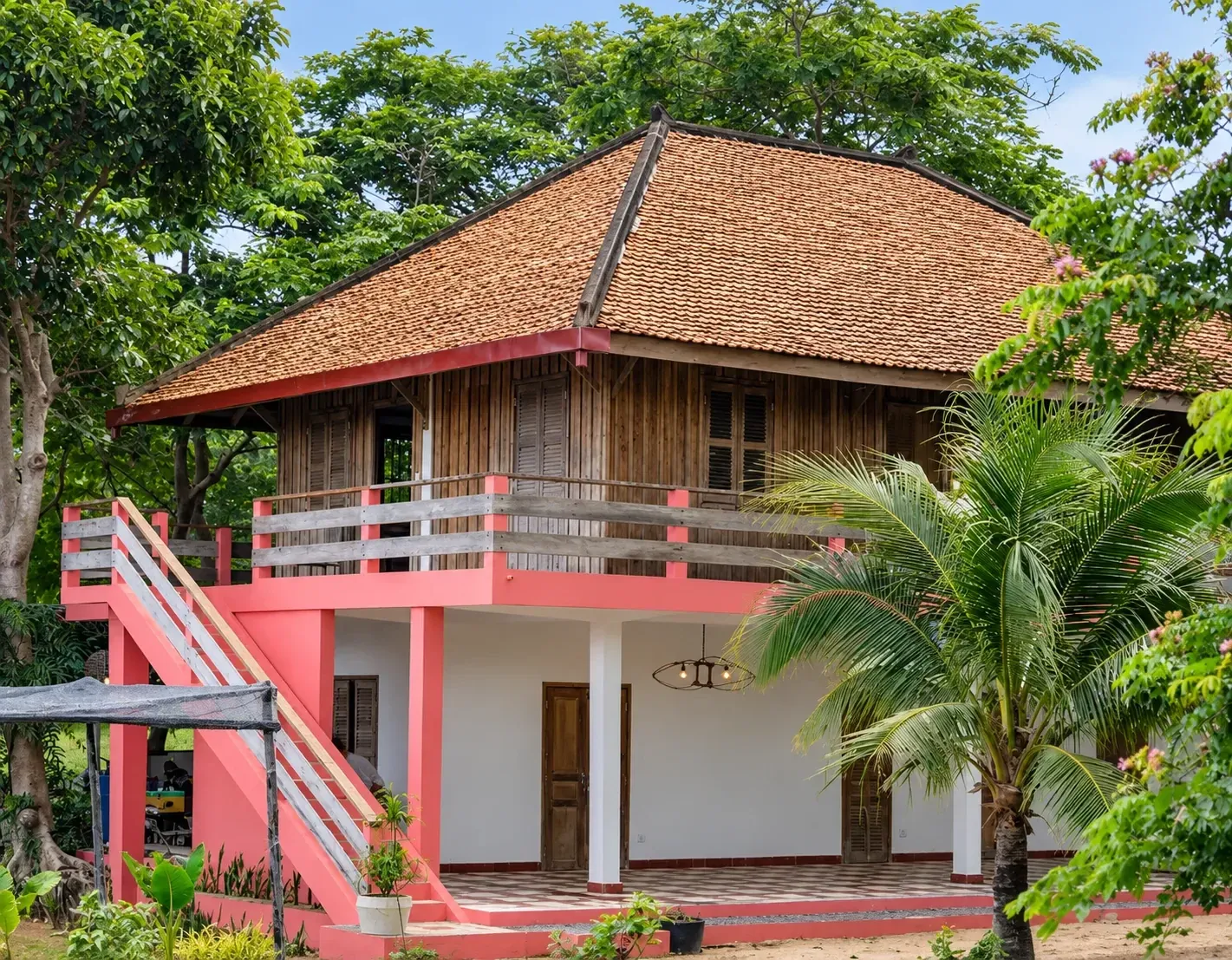 The Art for Kep residency house, a two-storey wooden villa with a tiled roof and coral-pink stairs among palms